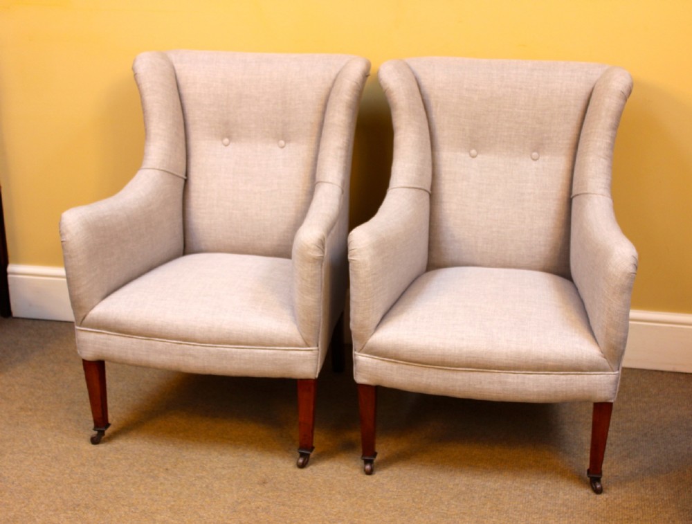 A pair of late nineteenth-century small wing armchairs upholstered in light grey fabric with tapered walnut legs on brass castors. View II