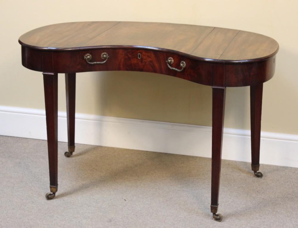 A Georgian mahogany kidney-shaped writing desk featuring tapered legs, brass castors, and a central drawer with brass handles. View II