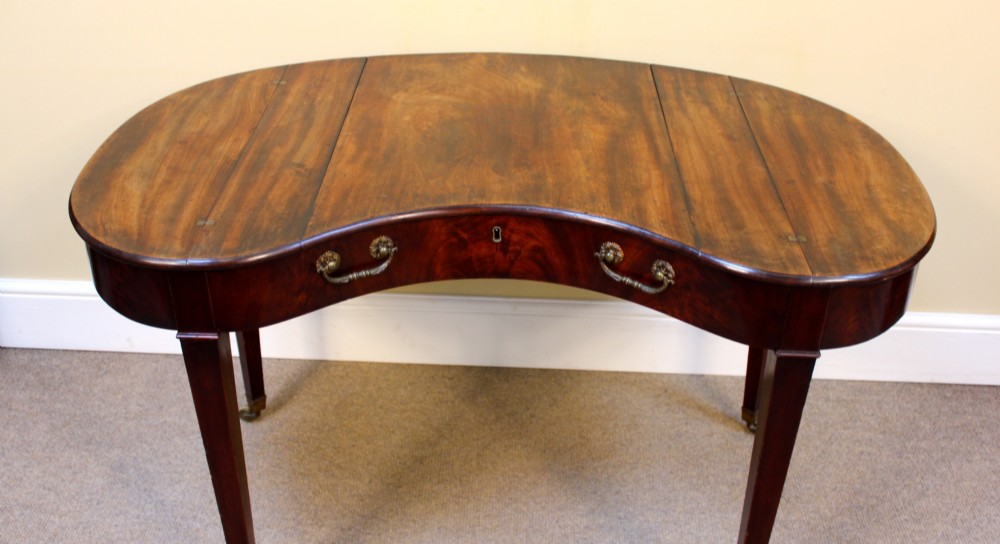 A Georgian mahogany kidney-shaped writing desk featuring tapered legs, brass castors, and a central drawer with brass handles. View III
