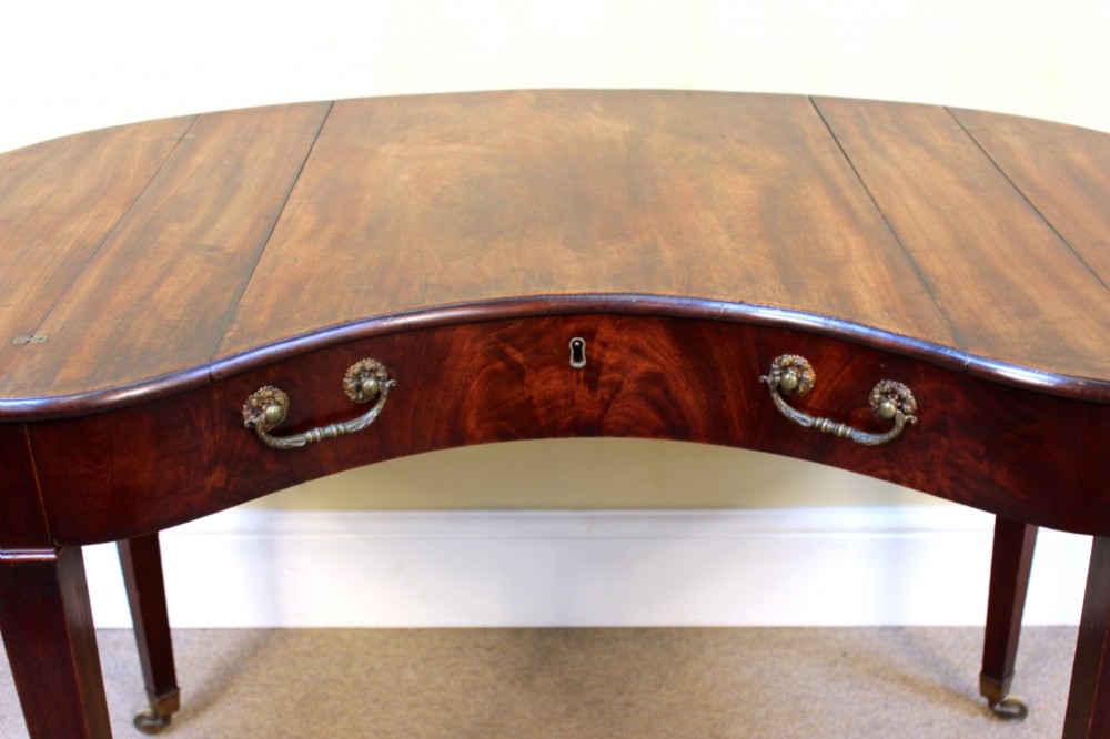 A Georgian mahogany kidney-shaped writing desk featuring tapered legs, brass castors, and a central drawer with brass handles. View IV