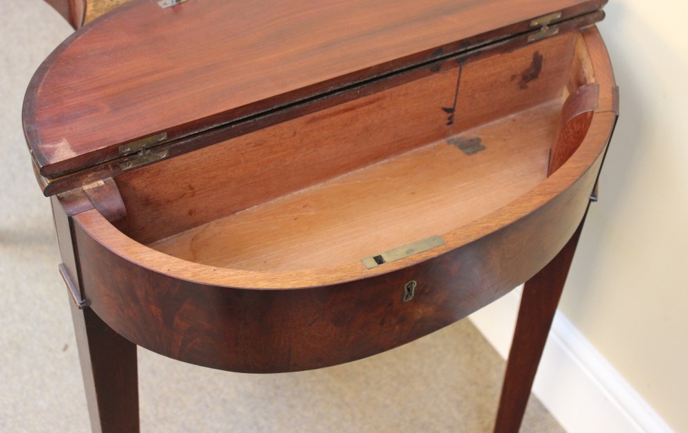 A Georgian mahogany kidney-shaped writing desk featuring tapered legs, brass castors, and a central drawer with brass handles. View VI