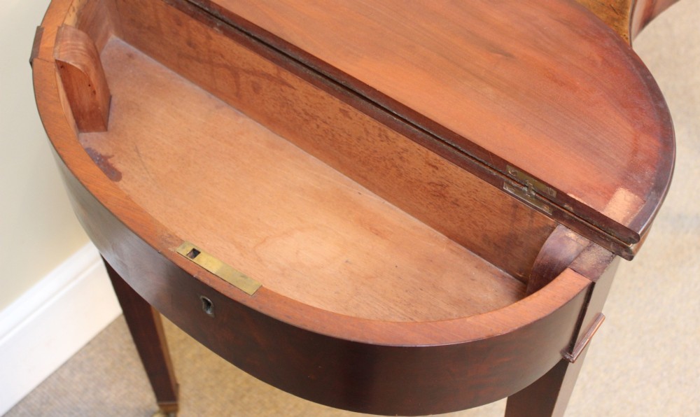 A Georgian mahogany kidney-shaped writing desk featuring tapered legs, brass castors, and a central drawer with brass handles. View VII