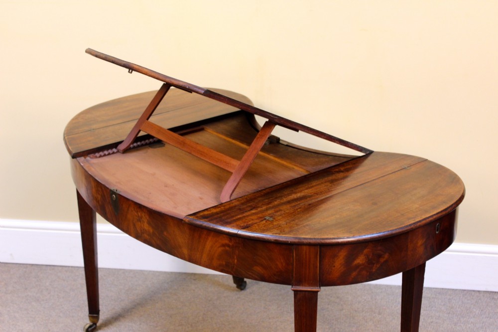 A Georgian mahogany kidney-shaped writing desk featuring tapered legs, brass castors, and a central drawer with brass handles. View IX