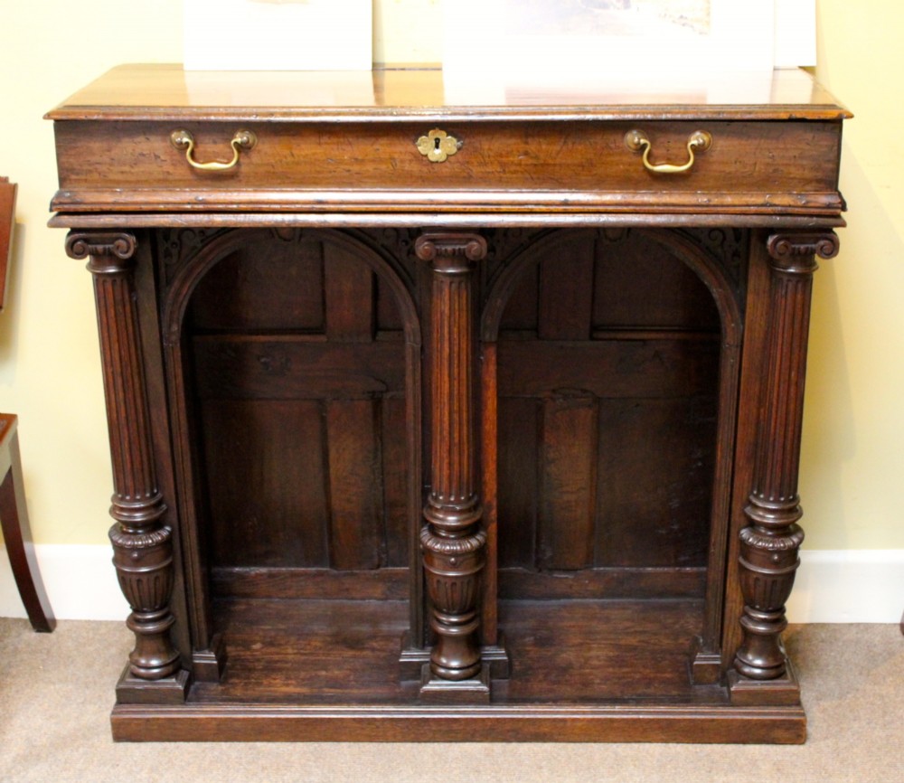 An 18th-century dark oak side table featuring a single top drawer with brass handles above twin open arched bays framed by fluted columns.