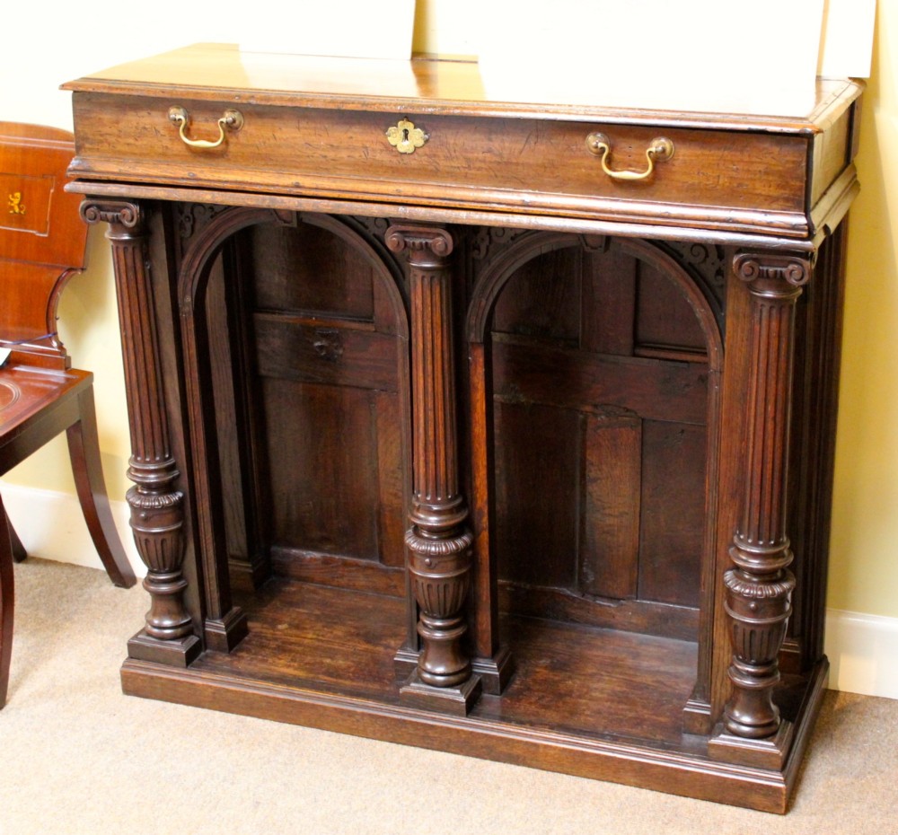 An 18th-century dark oak side table featuring a single top drawer with brass handles above twin open arched bays framed by fluted columns. View II