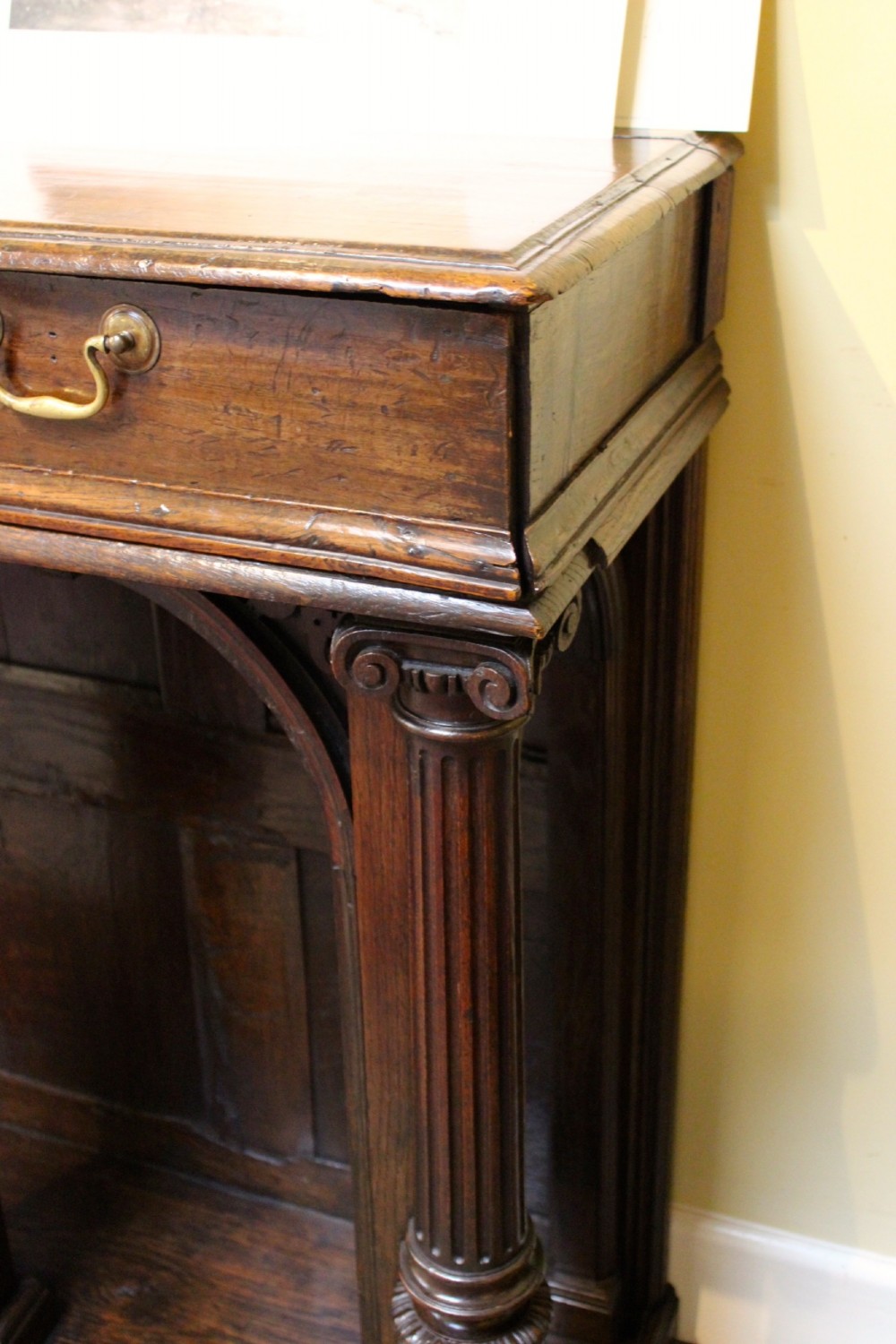 An 18th-century dark oak side table featuring a single top drawer with brass handles above twin open arched bays framed by fluted columns. View V