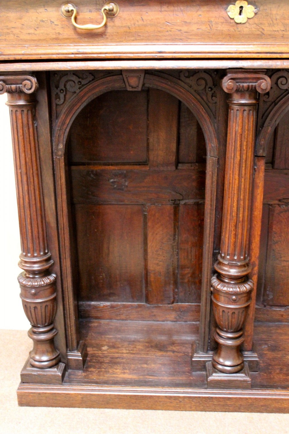 An 18th-century dark oak side table featuring a single top drawer with brass handles above twin open arched bays framed by fluted columns. View VII