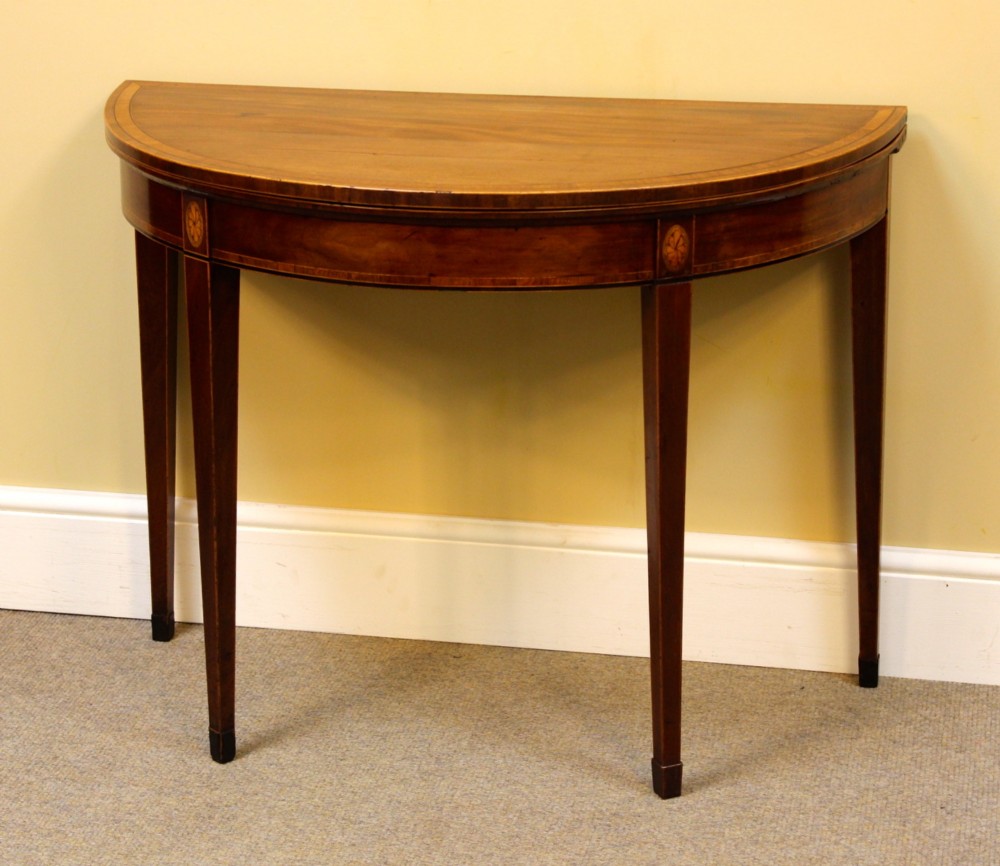 A Regency mahogany demilune card table with a folding top, satinwood stringing, oval patera inlays, and four tapered legs. View II