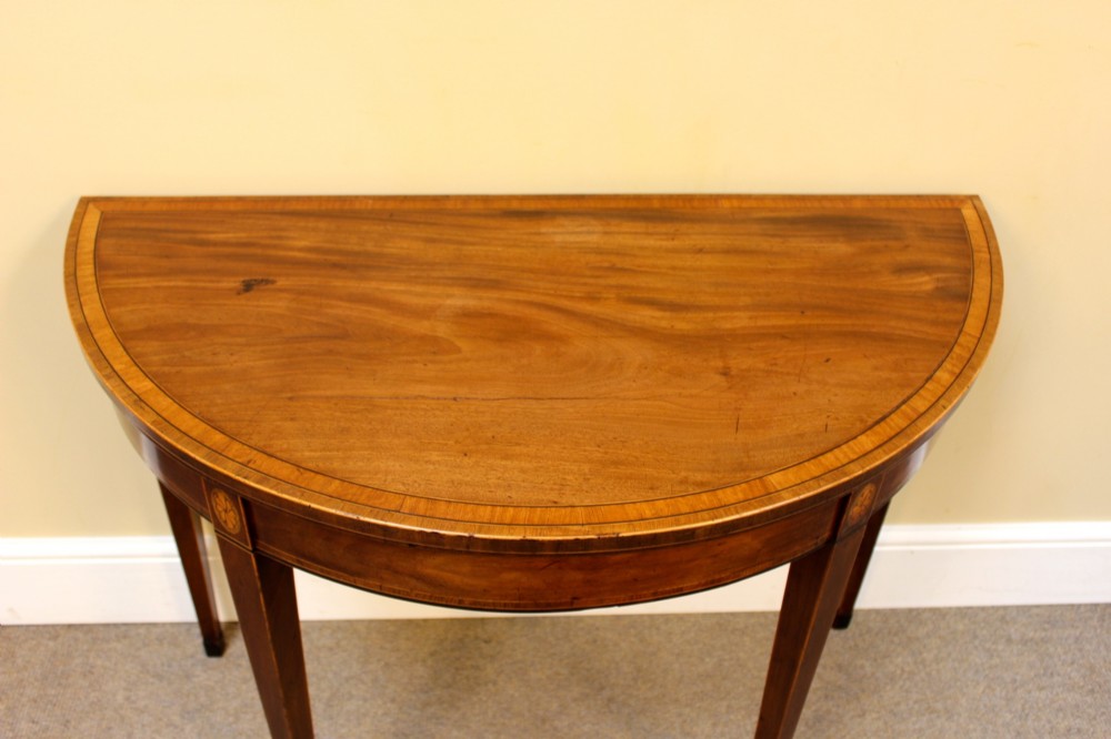 A Regency mahogany demilune card table with a folding top, satinwood stringing, oval patera inlays, and four tapered legs. View III