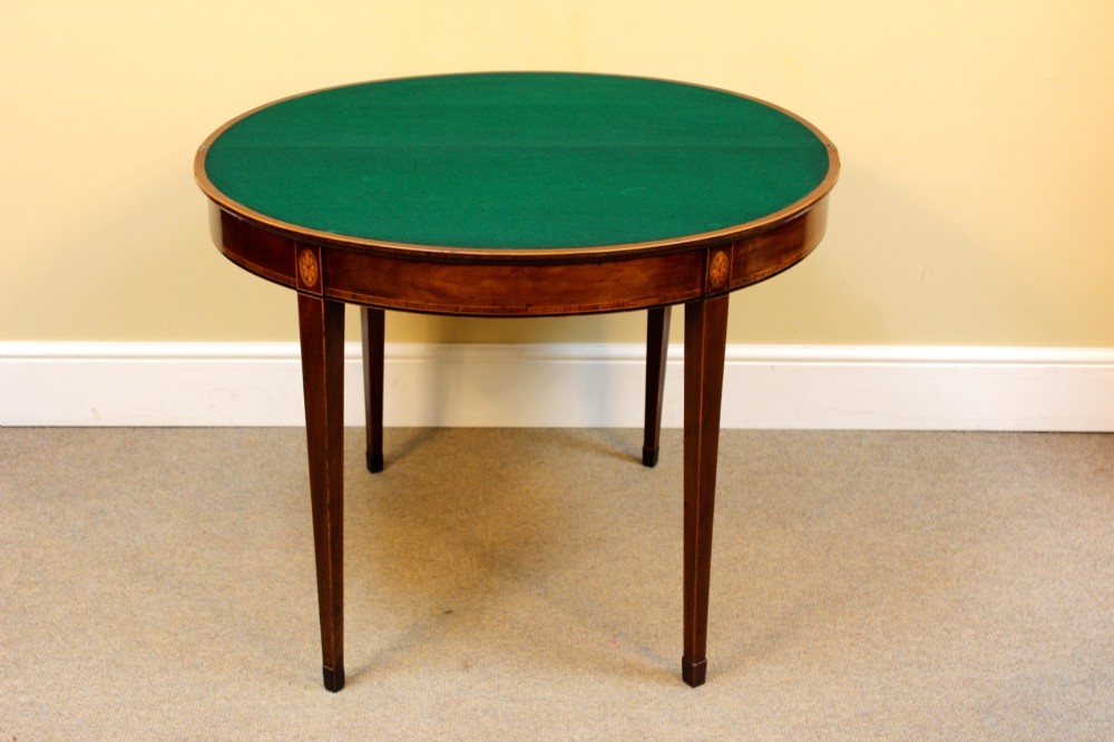 A Regency mahogany demilune card table with a folding top, satinwood stringing, oval patera inlays, and four tapered legs. View IV