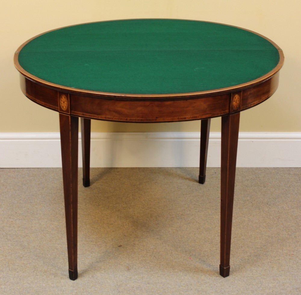 A Regency mahogany demilune card table with a folding top, satinwood stringing, oval patera inlays, and four tapered legs. View V