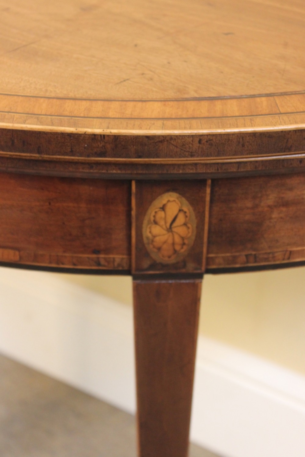 A Regency mahogany demilune card table with a folding top, satinwood stringing, oval patera inlays, and four tapered legs. View VI