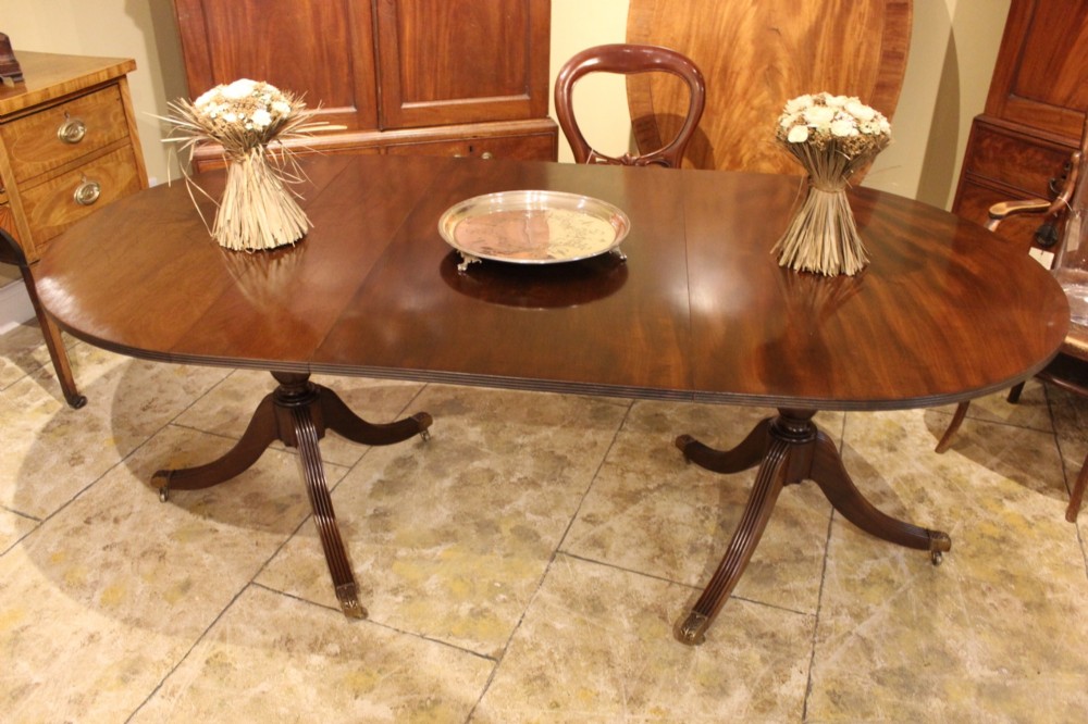 A 19th-century mahogany D-end extending dining table supported on twin turned pedestals with reeded splayed legs and brass castors. View II