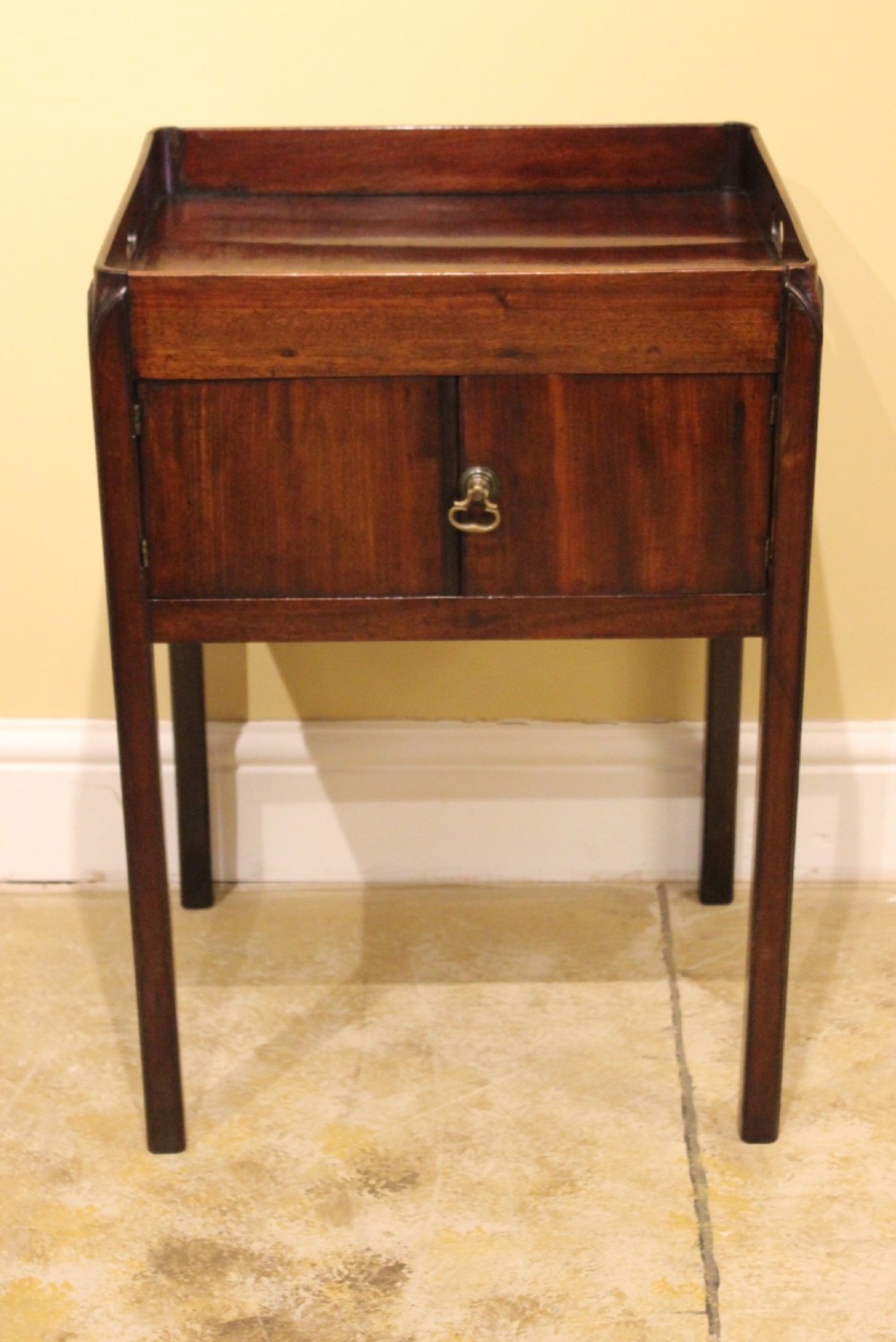 An antique Georgian mahogany bedside table featuring a tray top with cut-out hand-holds, double cupboard doors, a brass pull handle, and straight square legs. View III