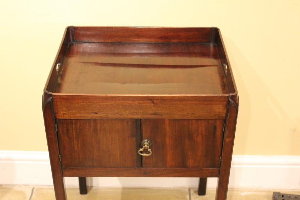 An antique Georgian mahogany bedside table featuring a tray top with cut-out hand-holds, double cupboard doors, a brass pull handle, and straight square legs. View IV