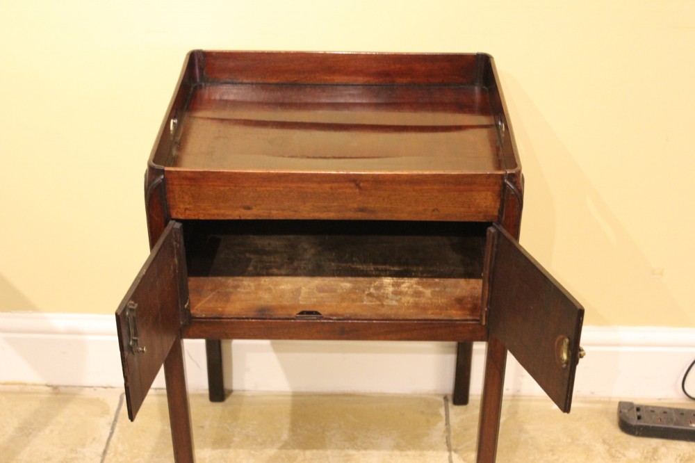 An antique Georgian mahogany bedside table featuring a tray top with cut-out hand-holds, double cupboard doors, a brass pull handle, and straight square legs. View V