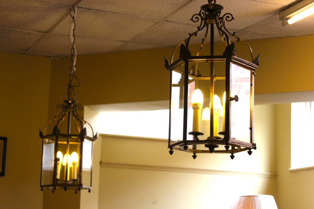 A pair of early twentieth-century hexagonal brass hanging lanterns featuring clear glass panes, scrollwork crowns, and internal multi-candle light sockets.