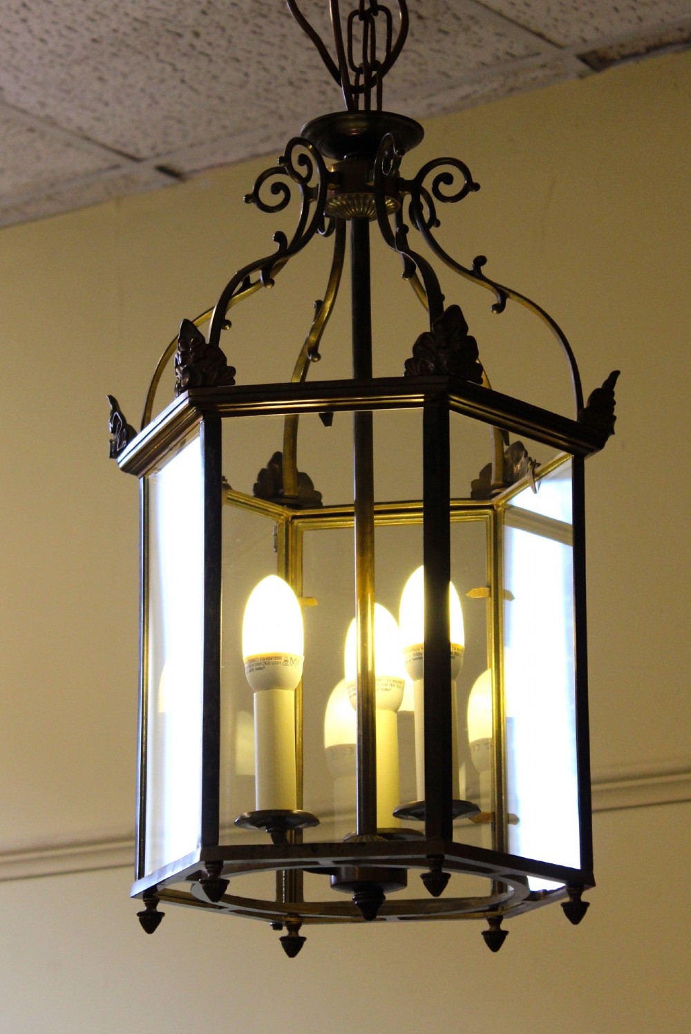 A pair of early twentieth-century hexagonal brass hanging lanterns featuring clear glass panes, scrollwork crowns, and internal multi-candle light sockets. View II