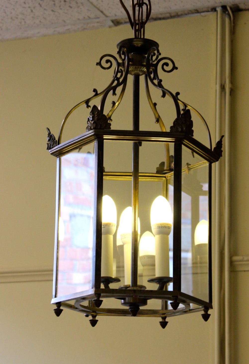 A pair of early twentieth-century hexagonal brass hanging lanterns featuring clear glass panes, scrollwork crowns, and internal multi-candle light sockets. View III