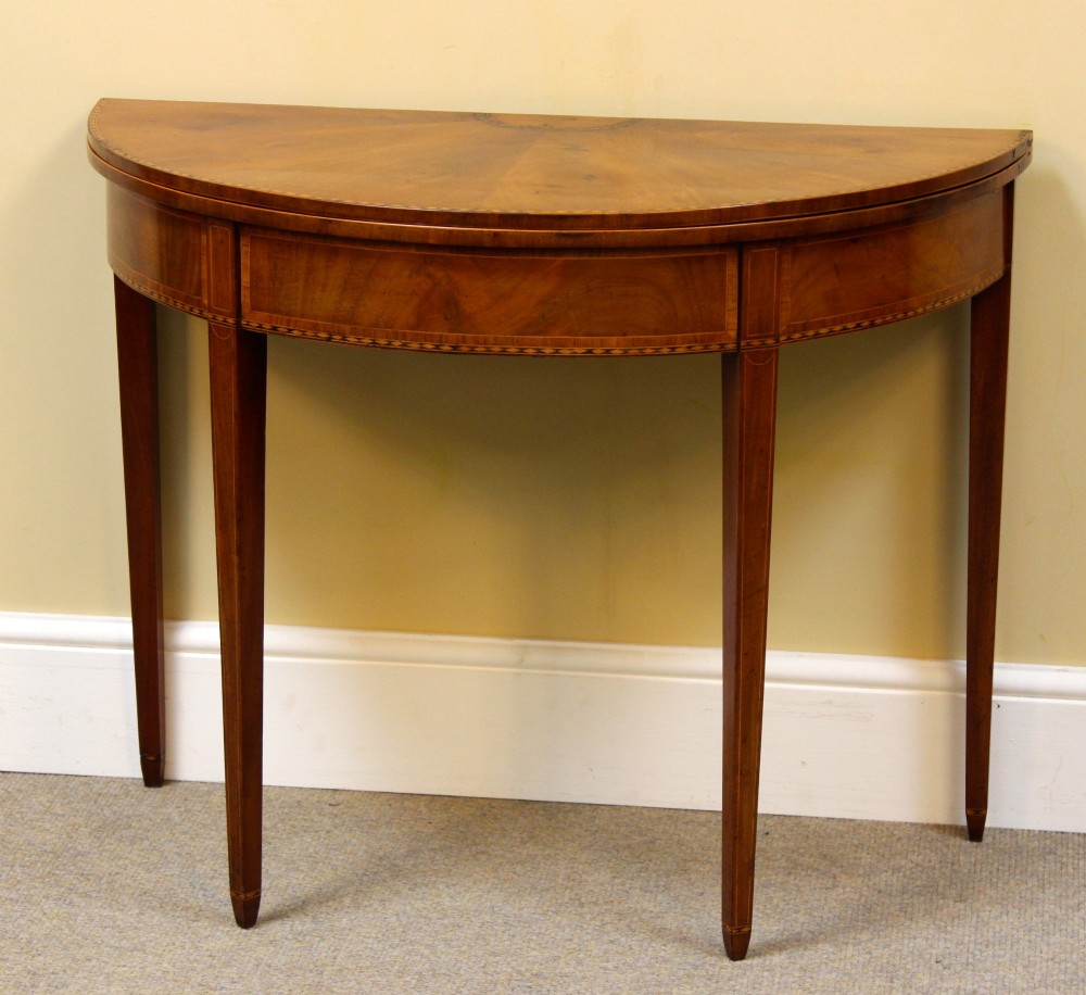 A 19th-century mahogany and fruitwood demi-lune card table featuring fan veneer inlays on the folding top and four tapered legs.