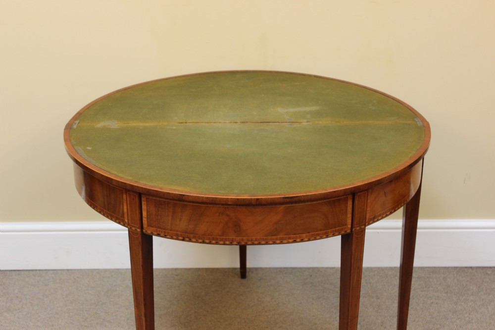 A 19th-century mahogany and fruitwood demi-lune card table featuring fan veneer inlays on the folding top and four tapered legs. View VII