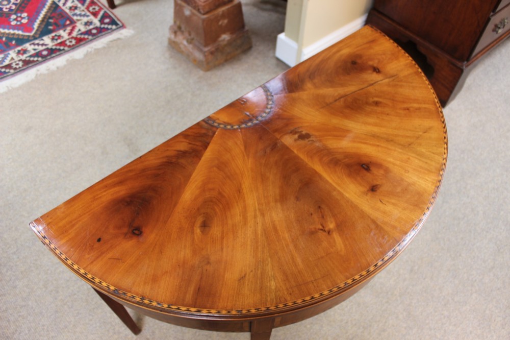 A 19th-century mahogany and fruitwood demi-lune card table featuring fan veneer inlays on the folding top and four tapered legs. View VIII