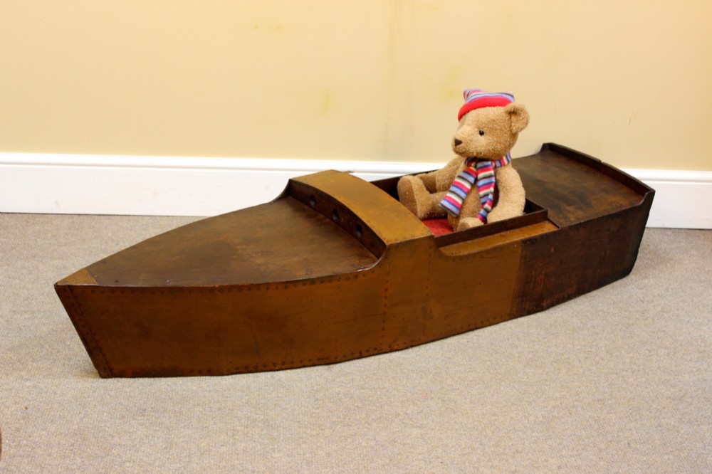 An Edwardian childs model speedboat crafted from brown patinated metal with riveted detailing, dashboard portholes, and a red interior seat. View III