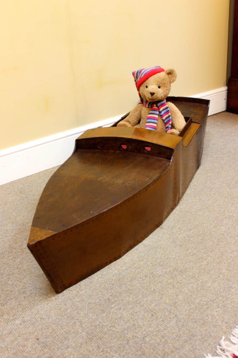 An Edwardian childs model speedboat crafted from brown patinated metal with riveted detailing, dashboard portholes, and a red interior seat. View IV
