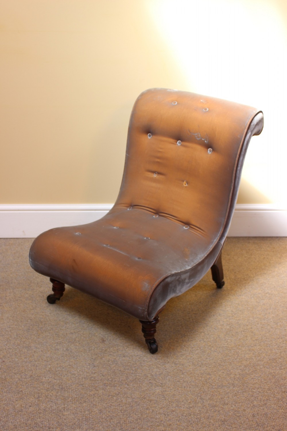 A 19th-century low-seated armless slipper chair upholstered in bronze brown fabric with button tufting on turned walnut legs with castors.