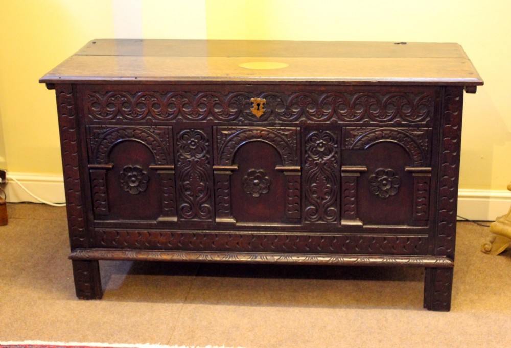 A dark carved oak coffer featuring three arcaded panels with carved floral details and a brass escutcheon. View II