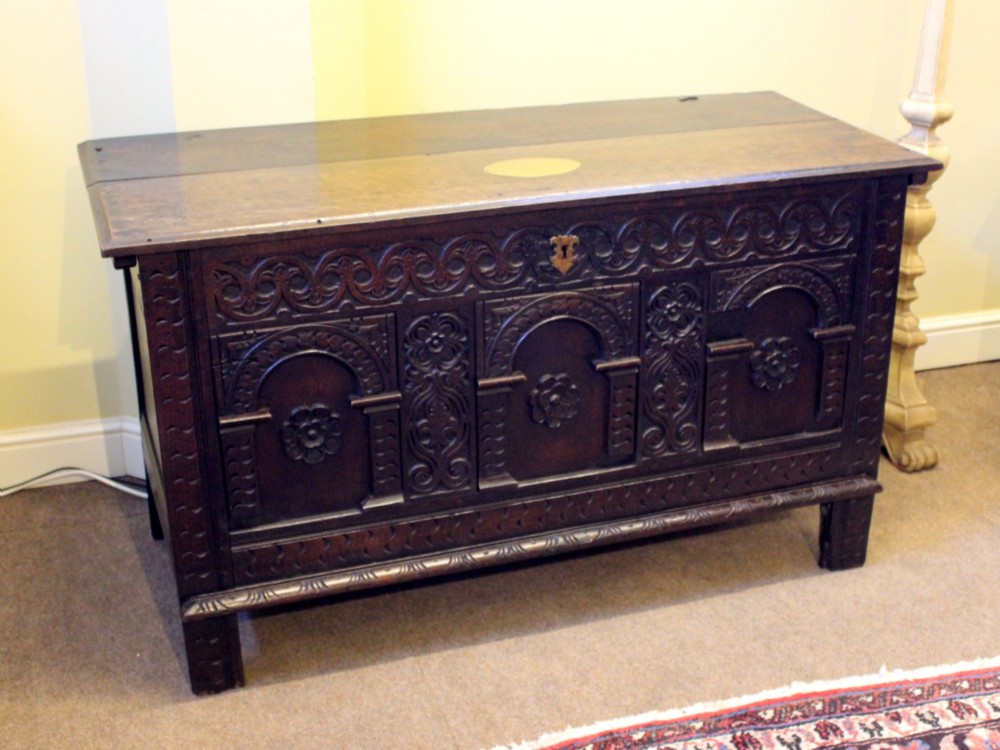 A dark carved oak coffer featuring three arcaded panels with carved floral details and a brass escutcheon. View III