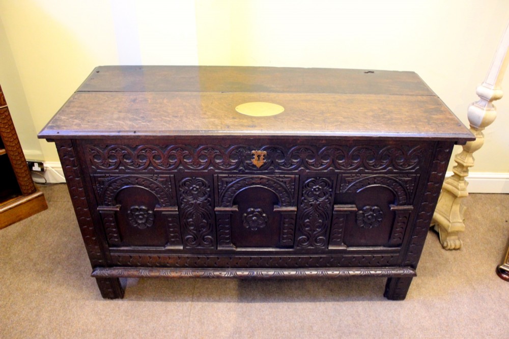 A dark carved oak coffer featuring three arcaded panels with carved floral details and a brass escutcheon. View IV