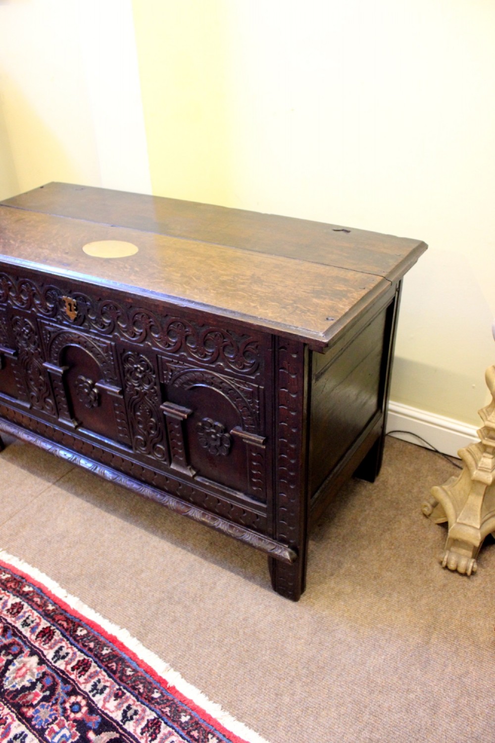 A dark carved oak coffer featuring three arcaded panels with carved floral details and a brass escutcheon. View V