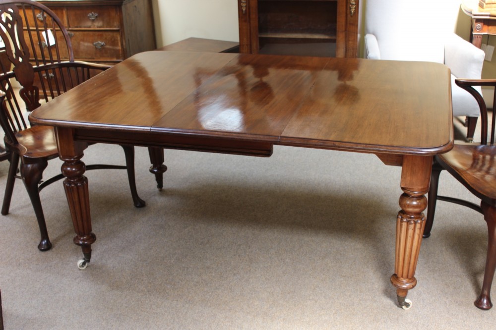 A nineteenth-century mahogany extending dining table with a polished rectangular top, rounded corners, and fluted turned legs on brass castors. View II