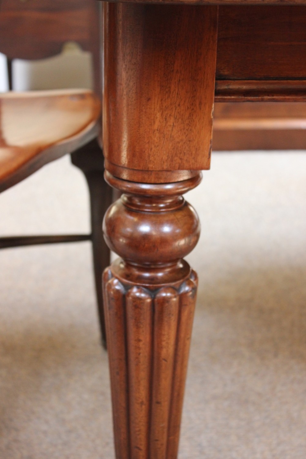 A nineteenth-century mahogany extending dining table with a polished rectangular top, rounded corners, and fluted turned legs on brass castors. View IV