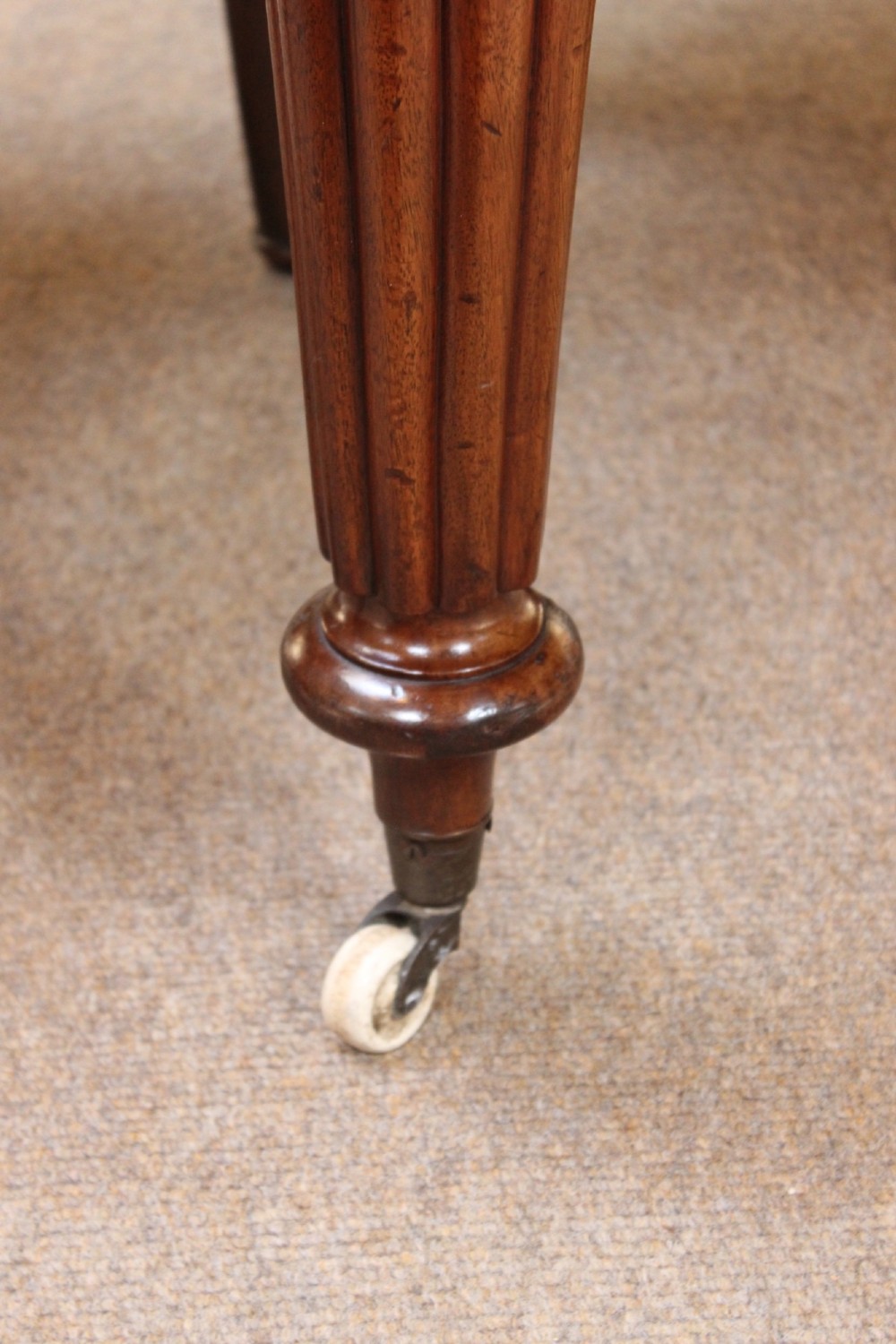 A nineteenth-century mahogany extending dining table with a polished rectangular top, rounded corners, and fluted turned legs on brass castors. View V