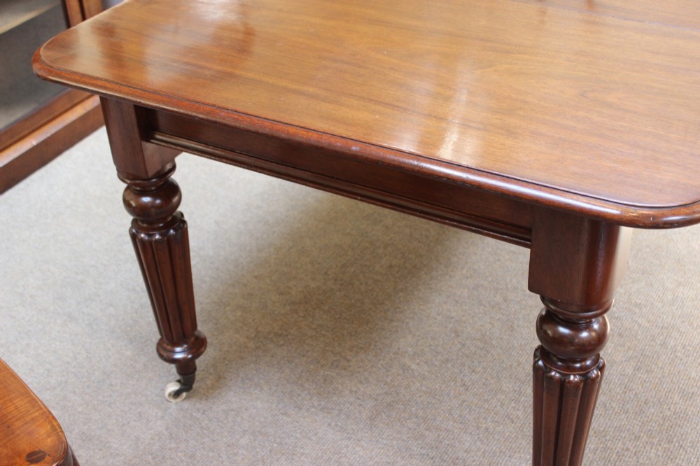 A nineteenth-century mahogany extending dining table with a polished rectangular top, rounded corners, and fluted turned legs on brass castors. View VI