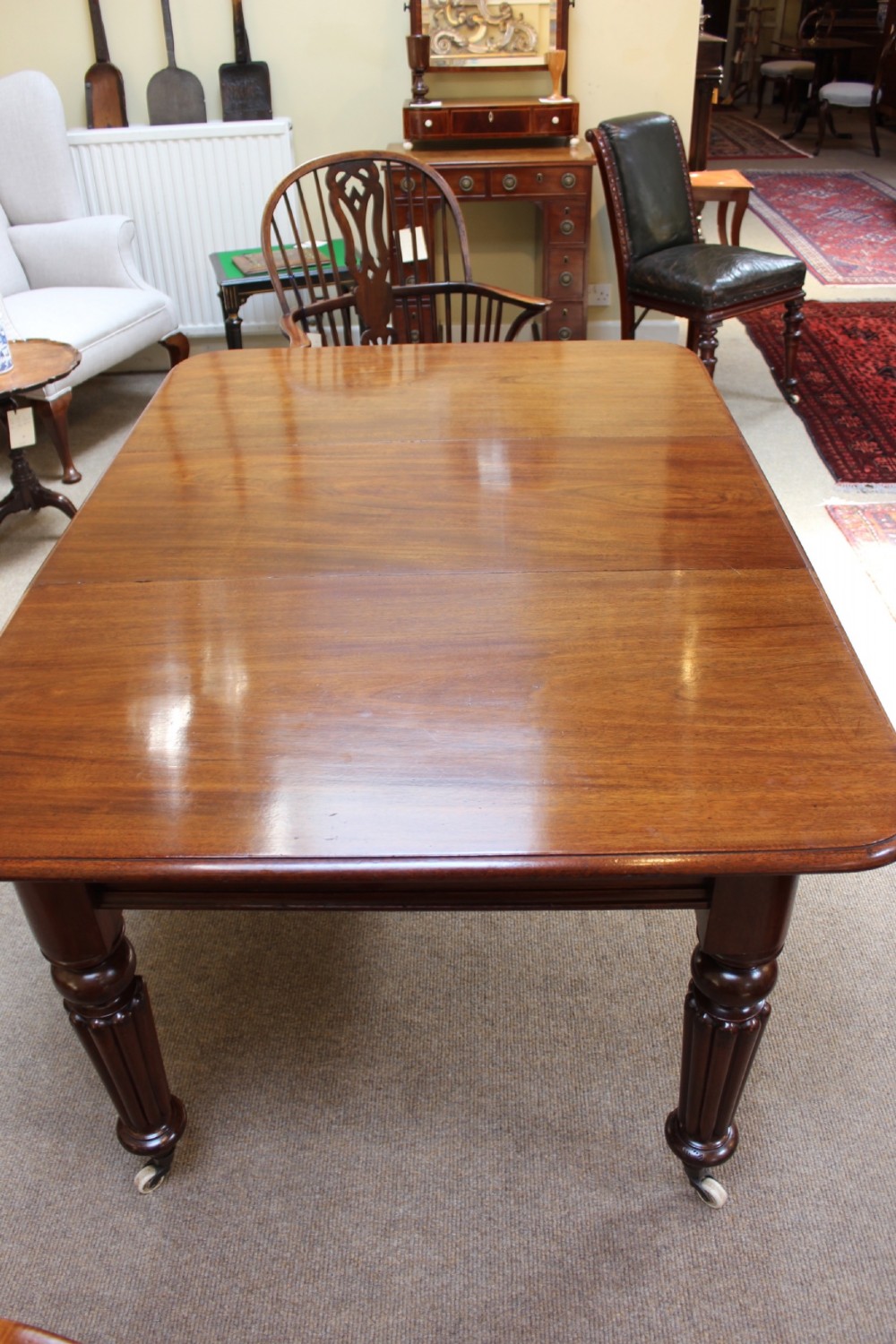 A nineteenth-century mahogany extending dining table with a polished rectangular top, rounded corners, and fluted turned legs on brass castors. View VII