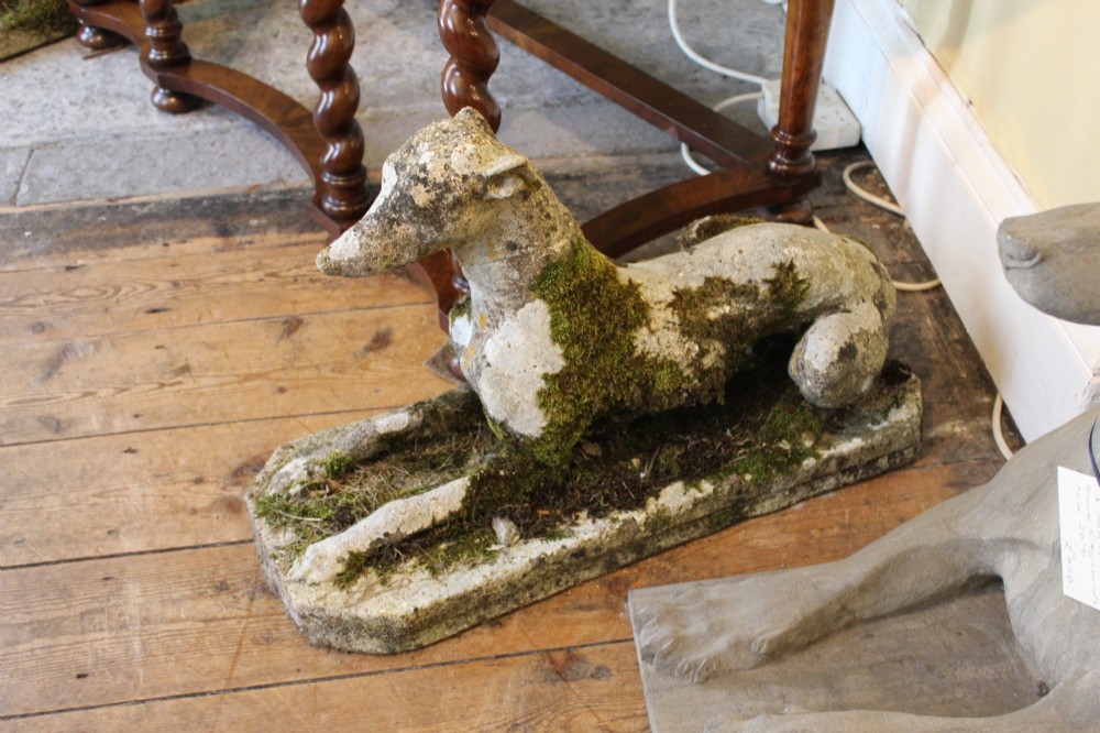 A pair of early 20th-century weathered cast stone statues depicting reclining whippets with natural moss growth on their surface. View II