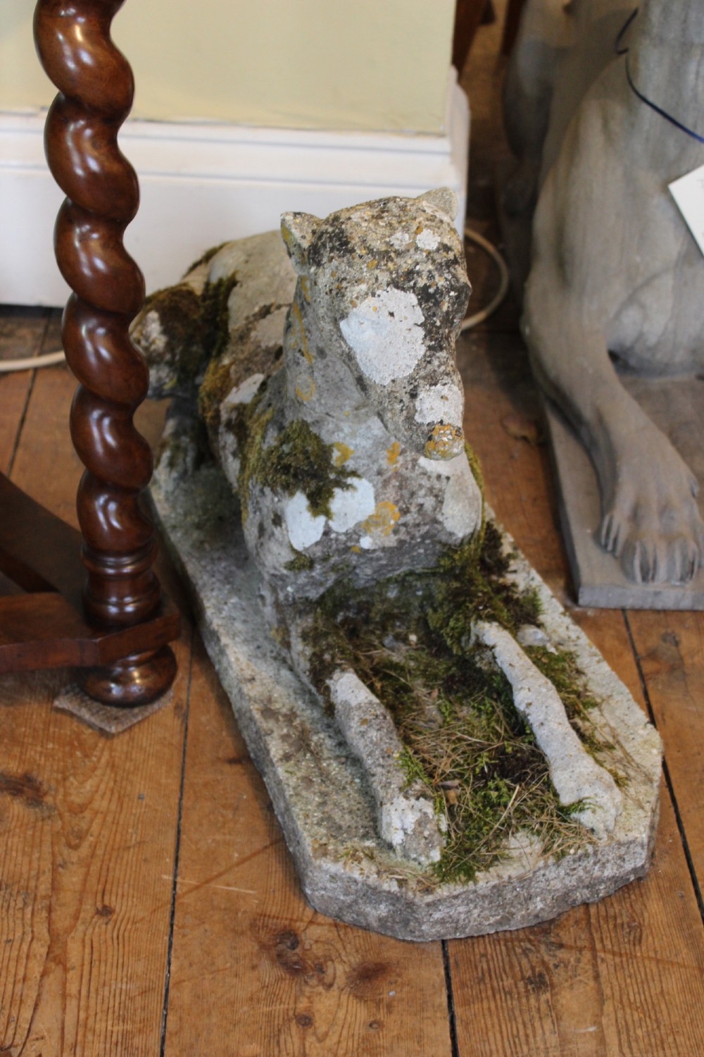 A pair of early 20th-century weathered cast stone statues depicting reclining whippets with natural moss growth on their surface. View IV