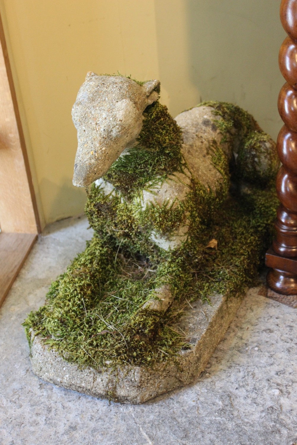 A pair of early 20th-century weathered cast stone statues depicting reclining whippets with natural moss growth on their surface. View V