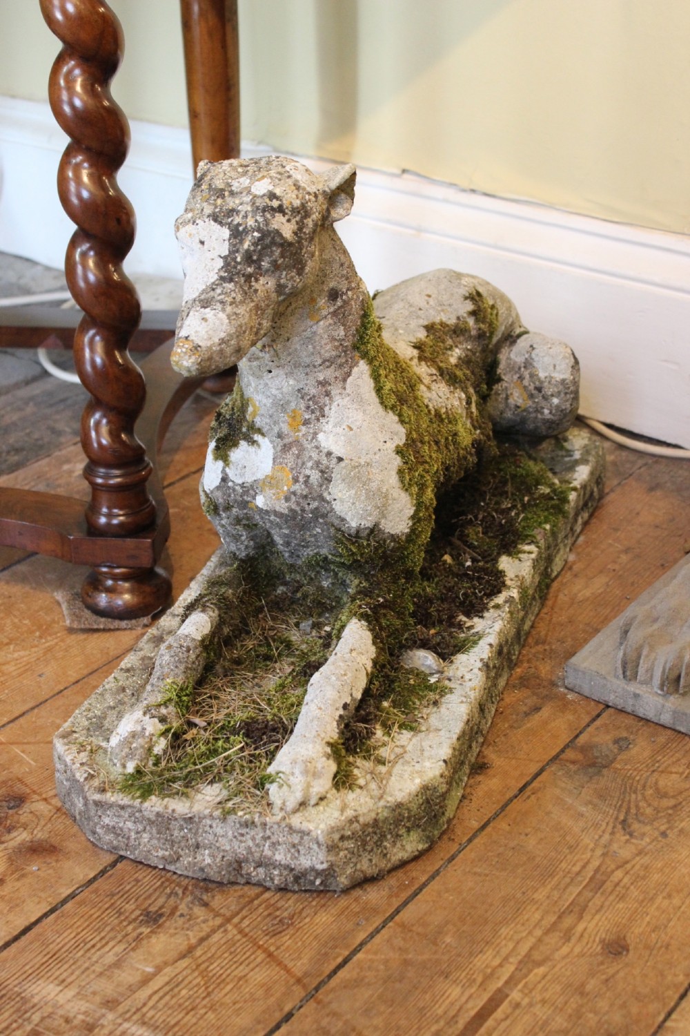A pair of early 20th-century weathered cast stone statues depicting reclining whippets with natural moss growth on their surface. View VI