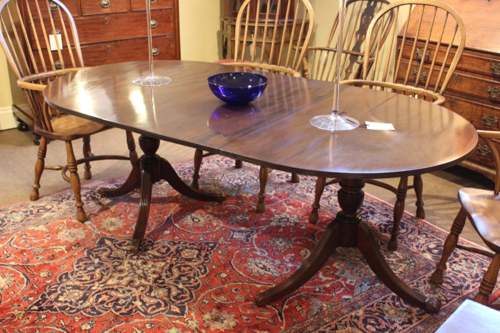 A late nineteenth-century mahogany twin-pillar dining table featuring an oval top supported by two turned pedestals with splayed reeded tripod legs.