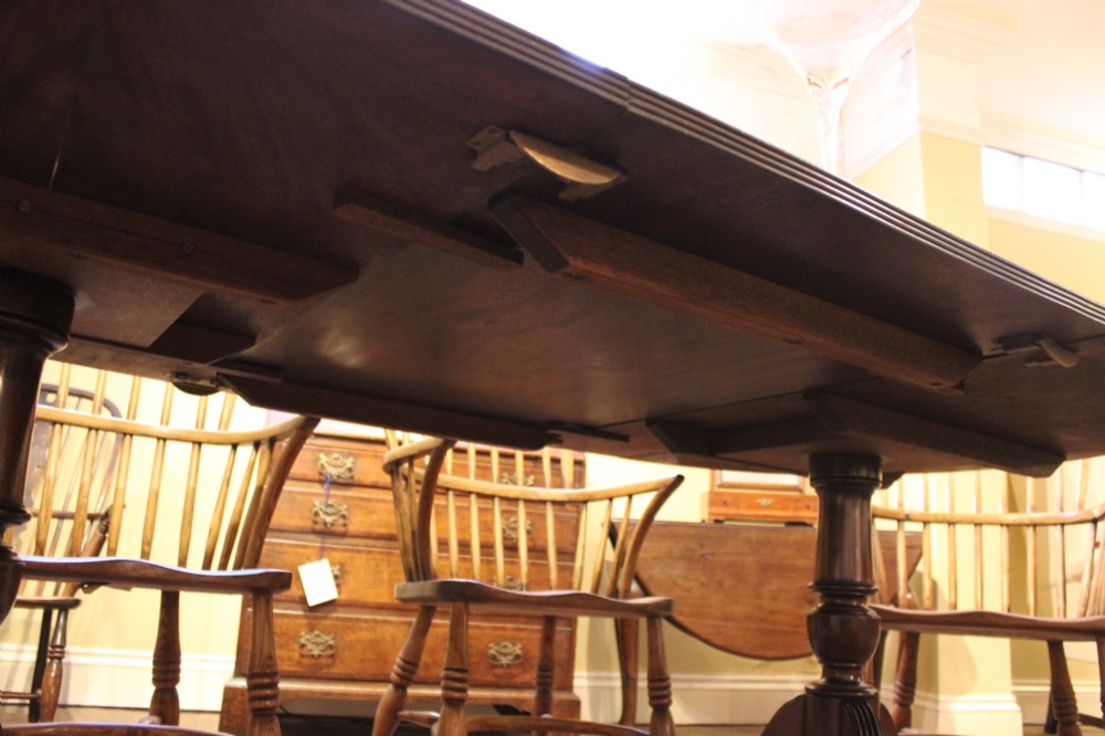 A late nineteenth-century mahogany twin-pillar dining table featuring an oval top supported by two turned pedestals with splayed reeded tripod legs. View VI