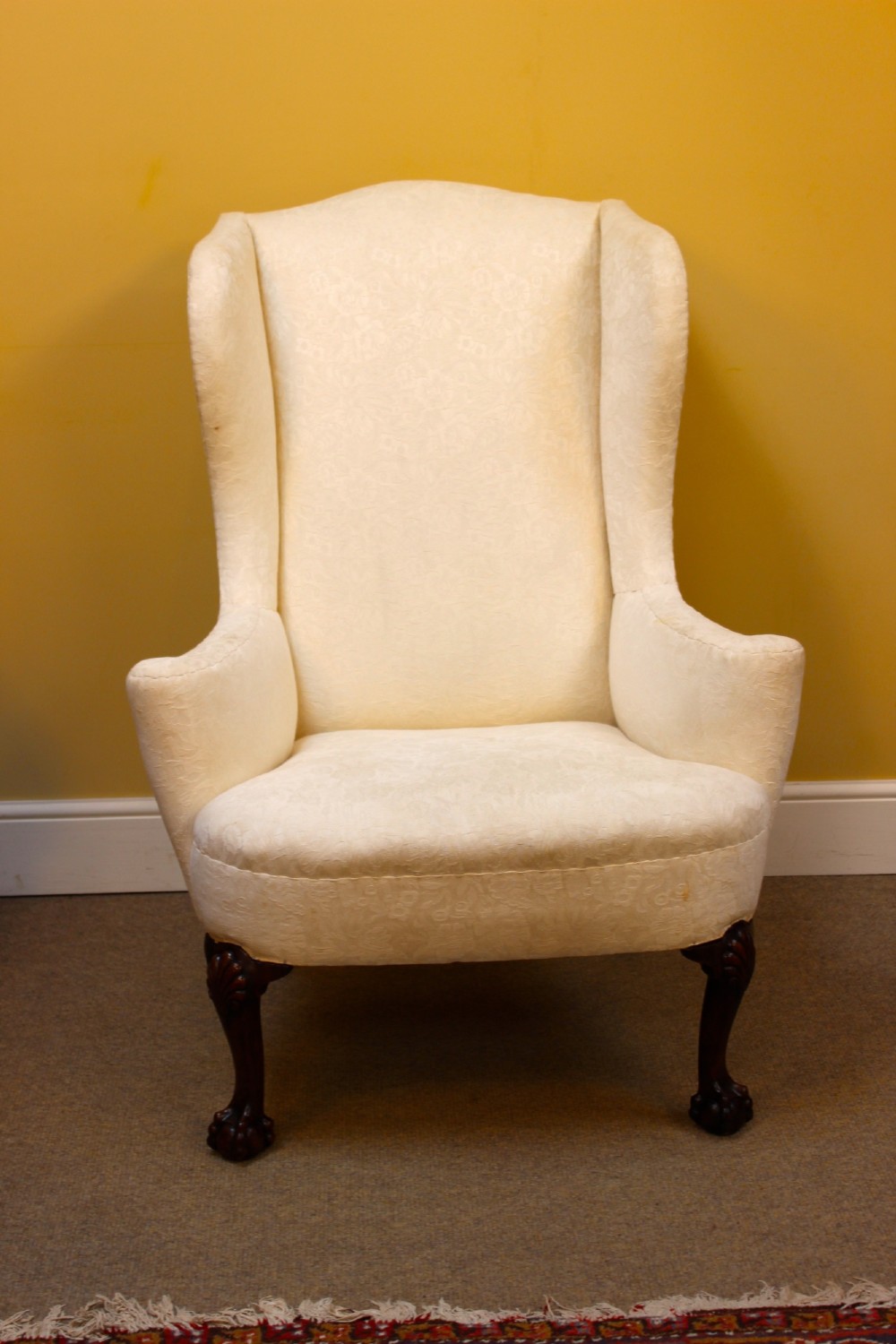 A 19th-century wingback armchair upholstered in cream patterned fabric featuring carved dark walnut cabriole front legs. View II