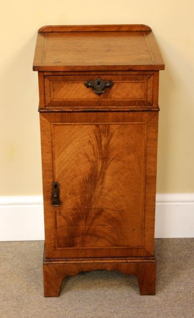 A late 19th-century walnut bedside cabinet featuring a top drawer, a single cupboard door with feather veneer grain, and brass hardware. View II