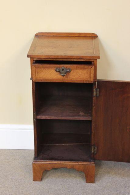 A late 19th-century walnut bedside cabinet featuring a top drawer, a single cupboard door with feather veneer grain, and brass hardware. View V