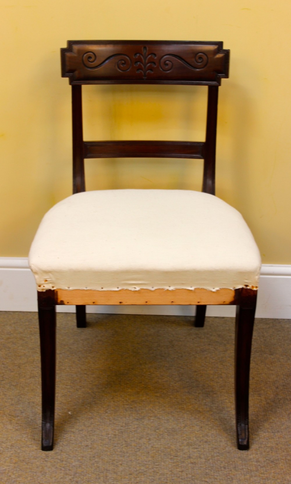 A nineteenth-century mahogany dining chair featuring a carved scroll crest rail, open back, cream upholstered seat, and tapered legs. View II