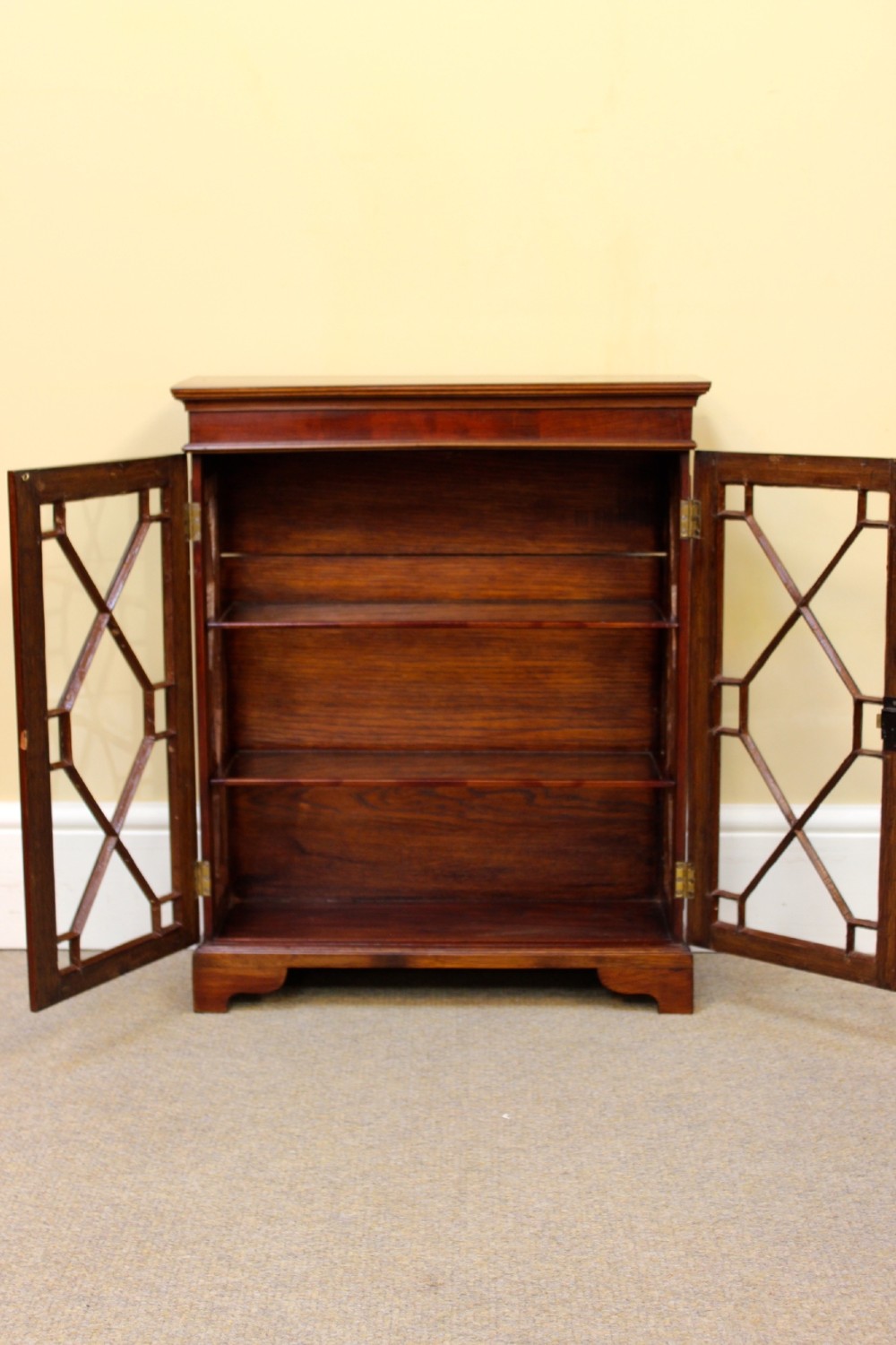 A 19th-century miniature mahogany display cabinet featuring twin astragal glazed doors and bracket feet. View V