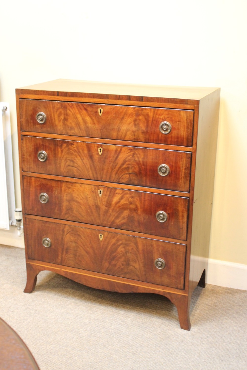 A nineteenth-century mahogany chest of four graduated drawers featuring flame mahogany grain and brass handles. View II